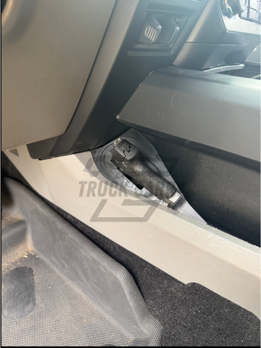 A close-up view of a truck interior door panel area showing a black plastic handle or latch component mounted near the floor, with a translucent protective sheet covering part of the area. A faint 'TRUCK' watermark is visible across the center.